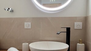 Un bagno moderno con uno specchio rotondo, un lavabo particolare e un asciugamano sul ripiano.