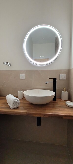 A modern bathroom with a round mirror, a large vessel sink, and a towel on the counter.