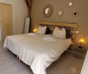 Una cama bien hecha con almohadas, una lámpara de noche y un espejo en la pared.
