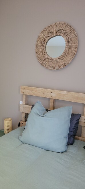 Un lit avec une tête de lit en bois, un miroir rond en osier et deux coussins.