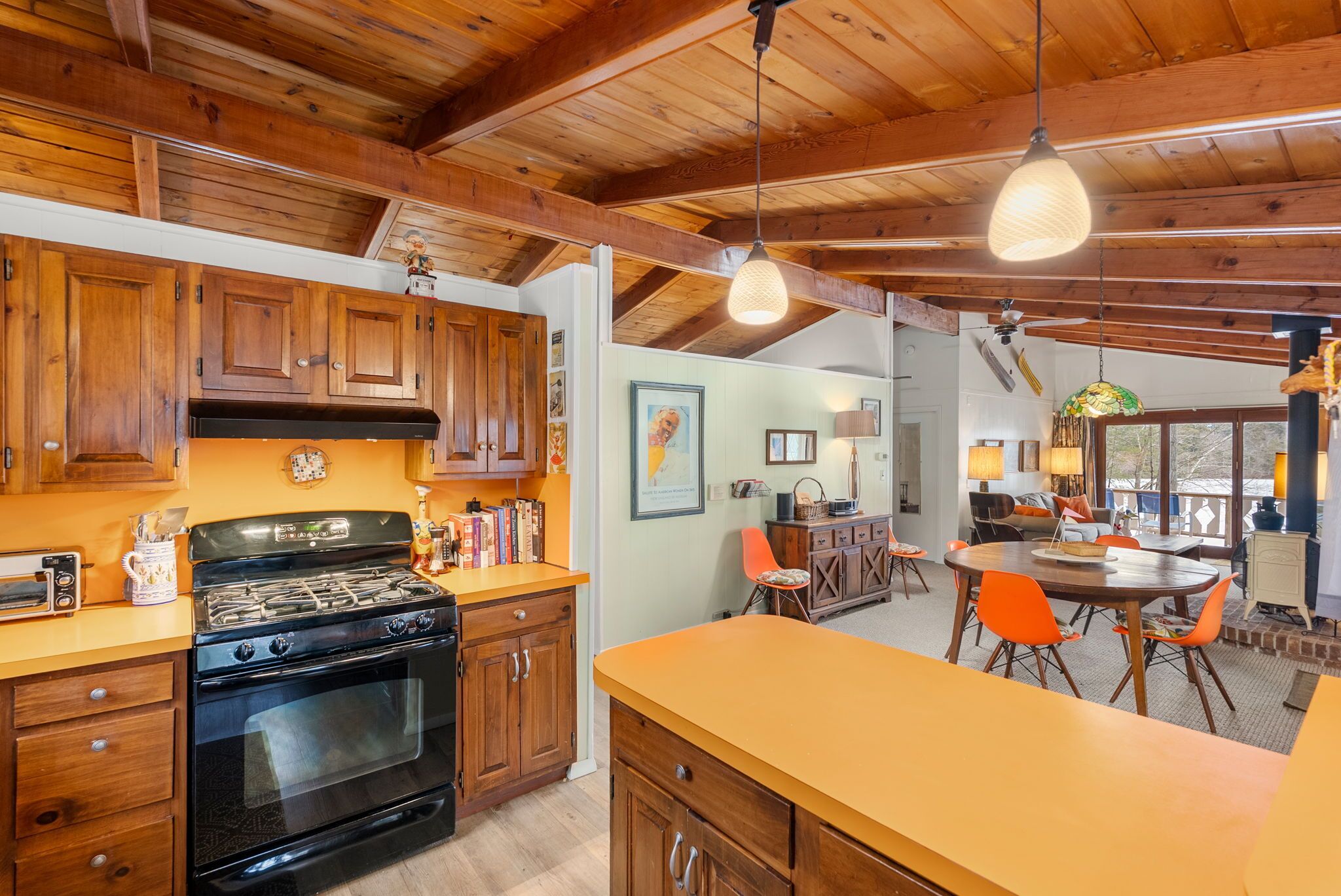 A kitchen with wooden cabinets, a stove, and a dining area with orange chairs.