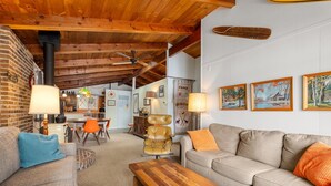 Uma sala de estar acolhedora com um sofá, uma mesa de centro de madeira, uma poltrona de couro e uma área de jantar com mesa e cadeiras.