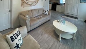 A living room with a sofa, a coffee table, a ceiling fan, and a kitchen in the background. - Dagsboro Retreat (Dagsboro)