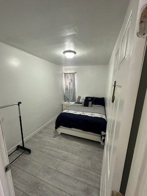 Une chambre Ă coucher avec un lit, une fenĂȘtre avec des rideaux, un luminaire au plafond et une porte.