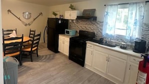 A compact kitchen with a dining table, chairs, a refrigerator, a stove, and a fire extinguisher. - Dagsboro Retreat (Dagsboro)
