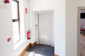 En gang med brandslukker, elevator og dør med nummer.