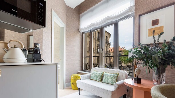 A modern kitchen with a microwave, kettle, and coffee maker. There is a white sofa with green cushions, a yellow trash bin, and a window with a view of buildings. - Exclusive Studio in Salamanca Isla de la Rua I (Salamanca)