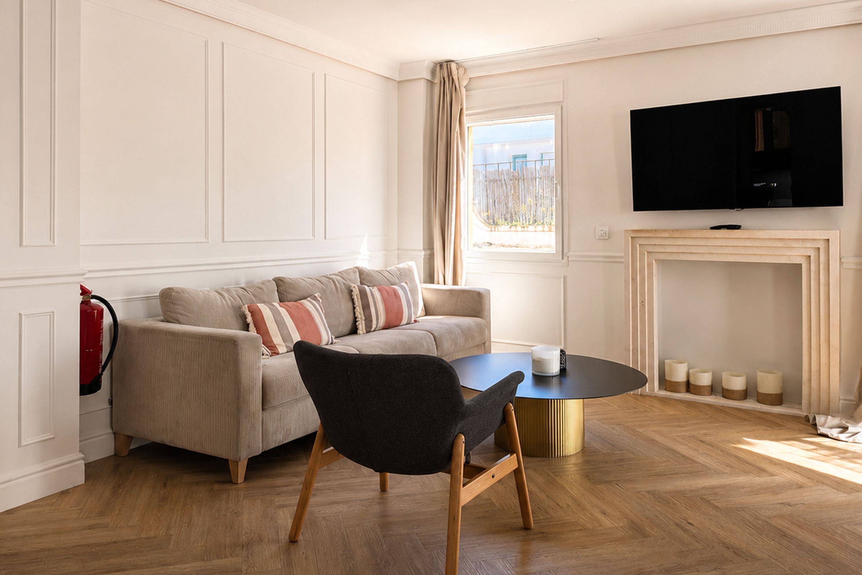 A living room with a sofa, a black chair, a round table, a fireplace, and a TV mounted on the wall.