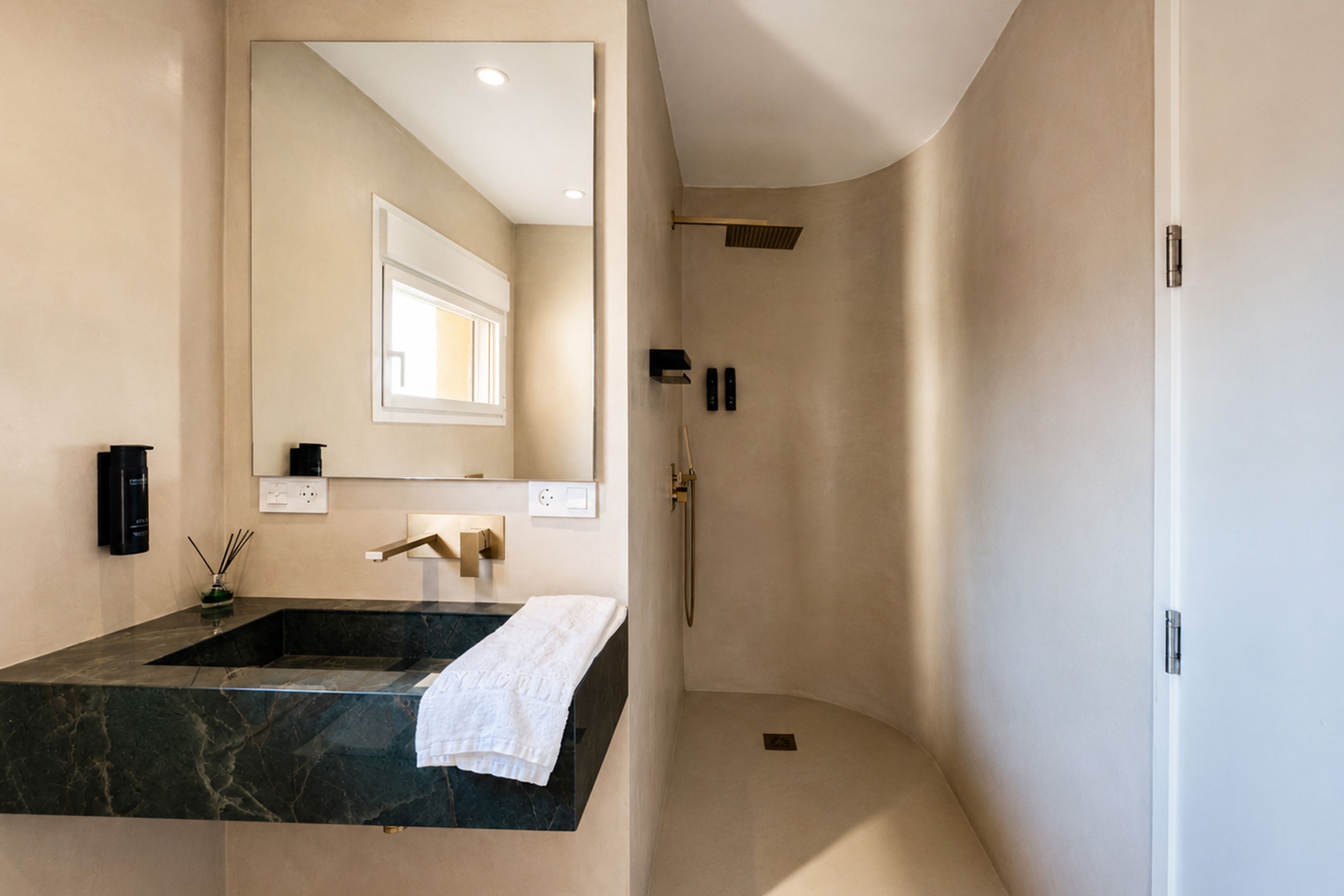Ein modernes Badezimmer mit großem Spiegel, Marmorwaschbecken in Schwarz, weißem Handtuch und Duschbereich.
