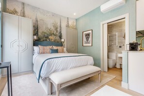 Una camera da letto con un letto, una panca, un armadio, un bagno e un angolo cottura.