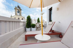 Een dakterras met een tafel en stoelen, een grote parasol en een klokkentoren op de achtergrond.