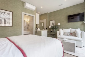 Una habitación de hotel moderna con una cama grande, un sofá, una mesita, un televisor y un espejo.