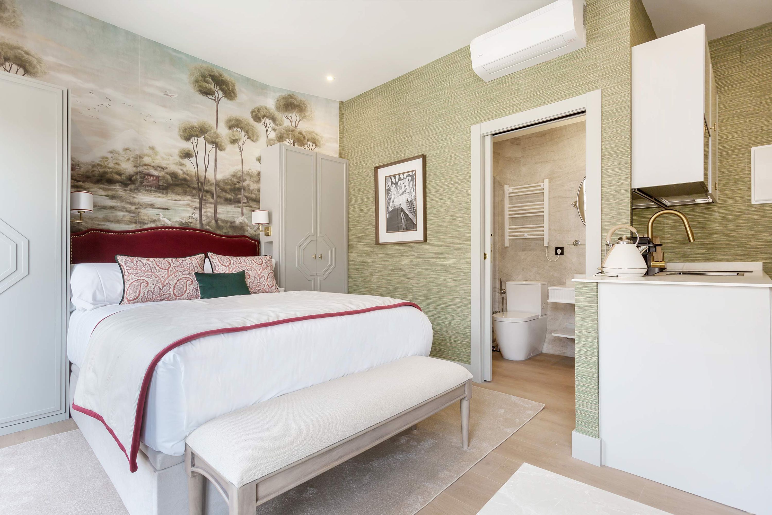 Quarto com cama, um banco e banheiro visível por uma porta aberta.