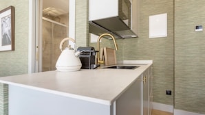 Una cocina compacta con cubierta blanca, hervidor, máquina de café y campana extractora de acero inoxidable.