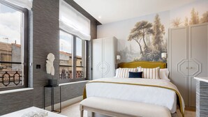 Un dormitorio con una cama grande, un banco, una mesa blanca y vistas al exterior.