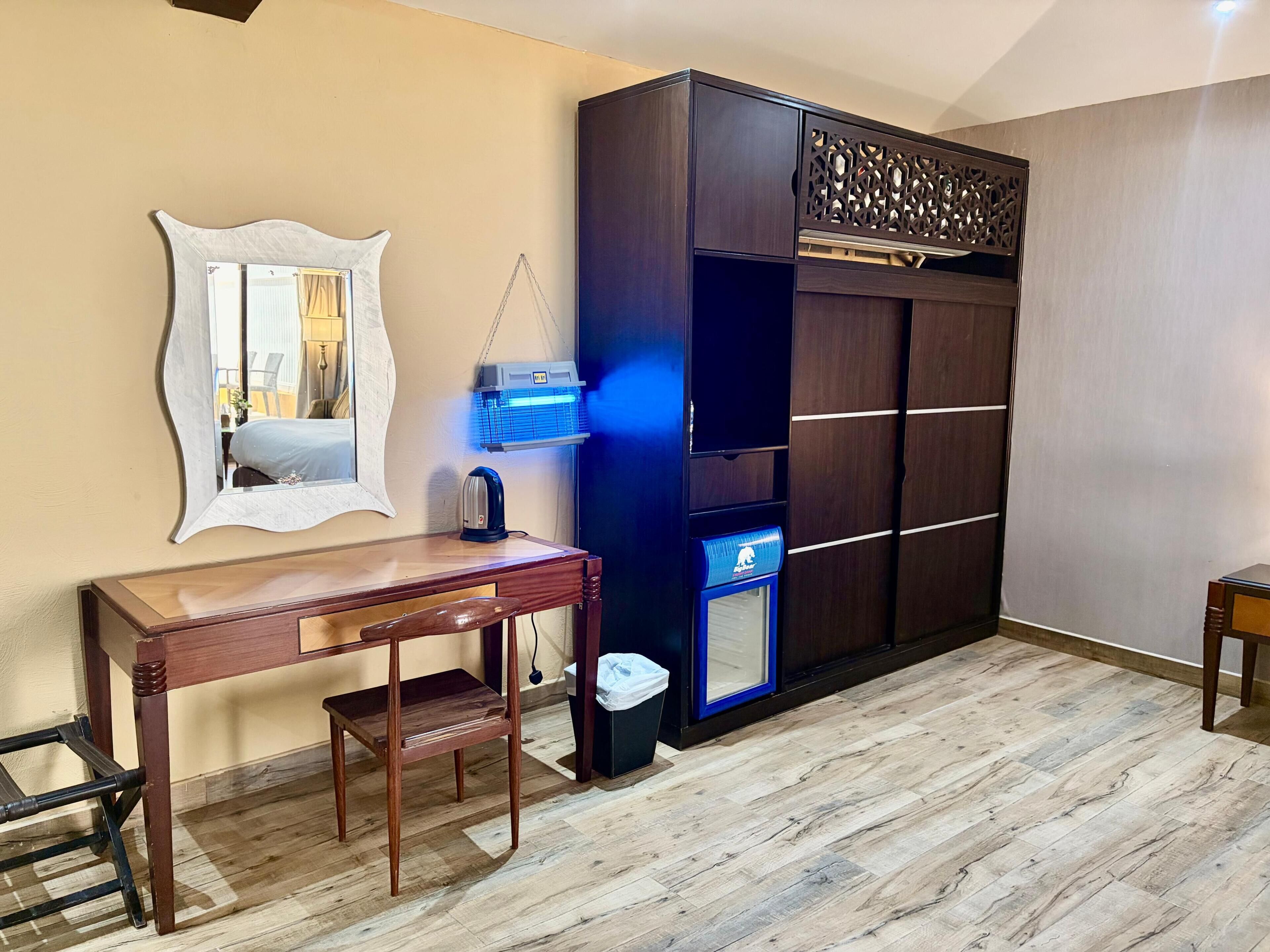 Une pièce comprenant un bureau en bois, un miroir, un radiateur et une armoire.
