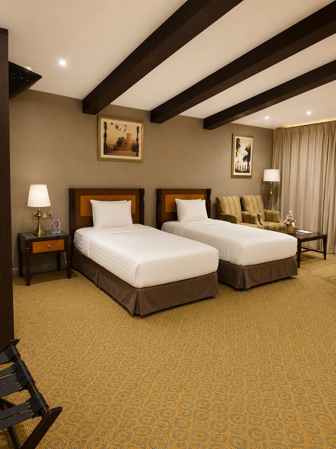 A hotel room with two beds, a desk, a chair, and a large window with curtains.