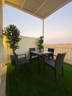 A covered outdoor area with a table and chairs, a potted plant, and a view of the beach.
