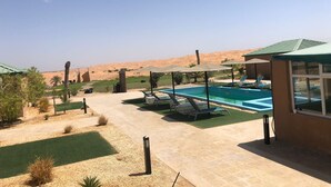 A pool area with lounge chairs, a small building, and a desert landscape in the background. - Desert Inn Resort and Camp (Ras Al Khaimah)