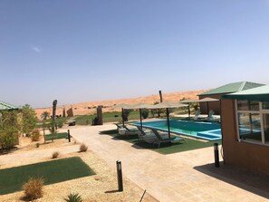A pool area with lounge chairs, a small building, and a desert landscape in the background.