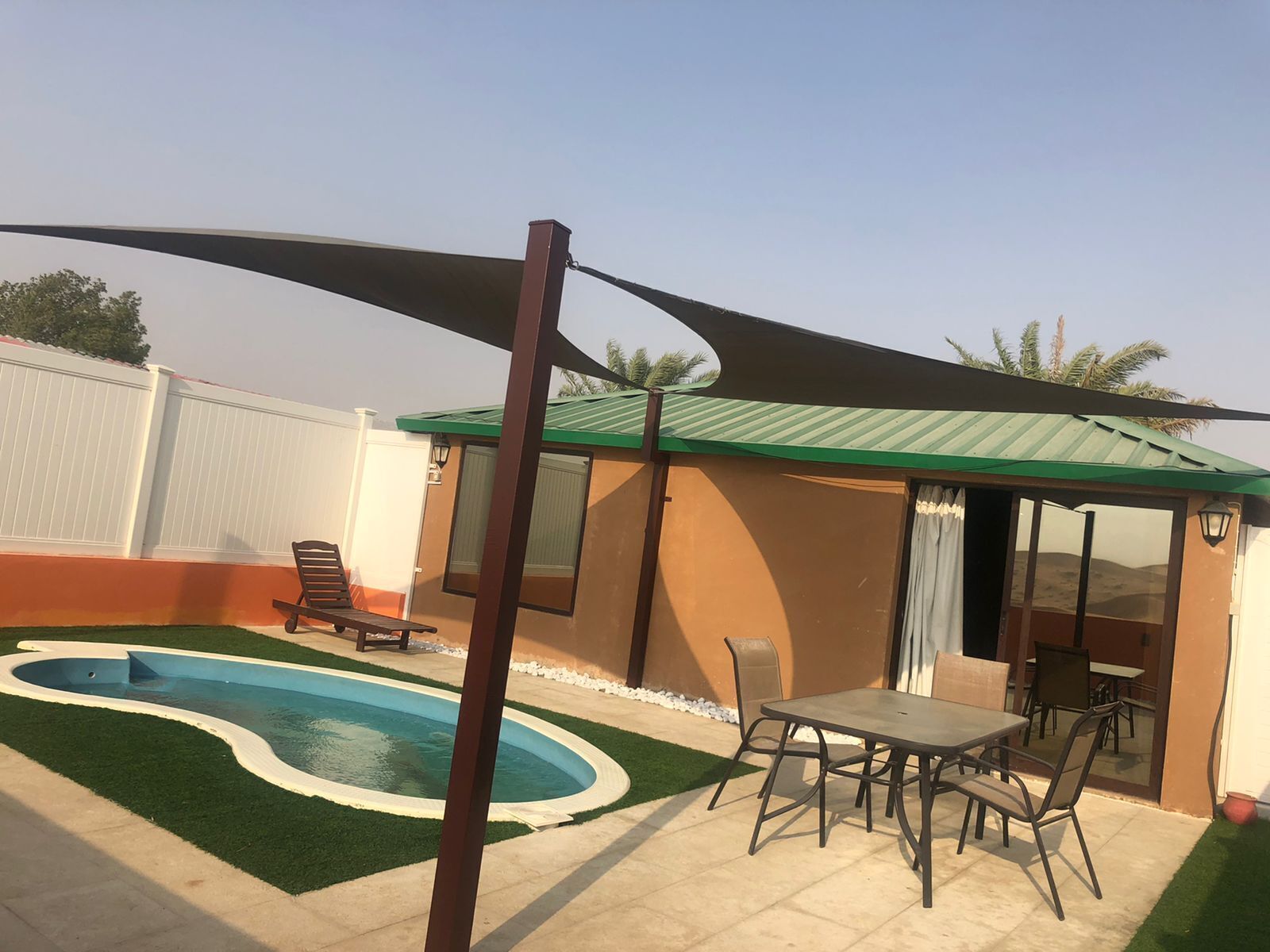A pool with a curved edge, a patio table with chairs, and a covered seating area.