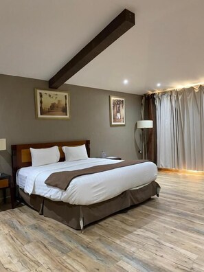 A hotel room with a large bed, wooden floor, and a ceiling beam.