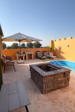 A patio with a stone fire pit, lounge chairs, and a pool.