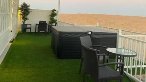 A covered outdoor area with a view of the desert, furnished with a table and chairs, and a sofa. - Desert Inn Resort and Camp (Ras Al Khaimah)