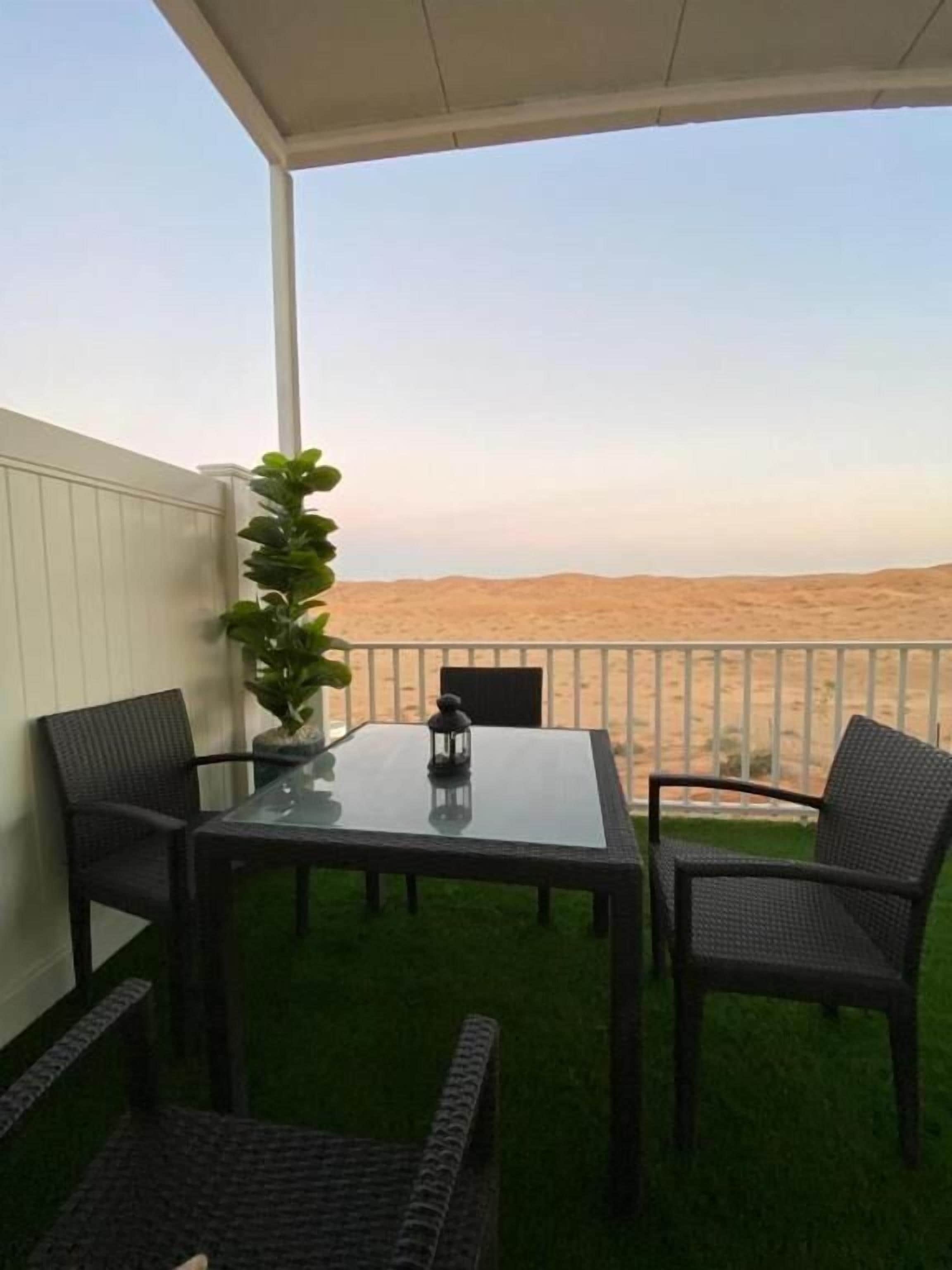 A covered outdoor seating area with a table and chairs, a potted plant, and a view of a desert landscape.