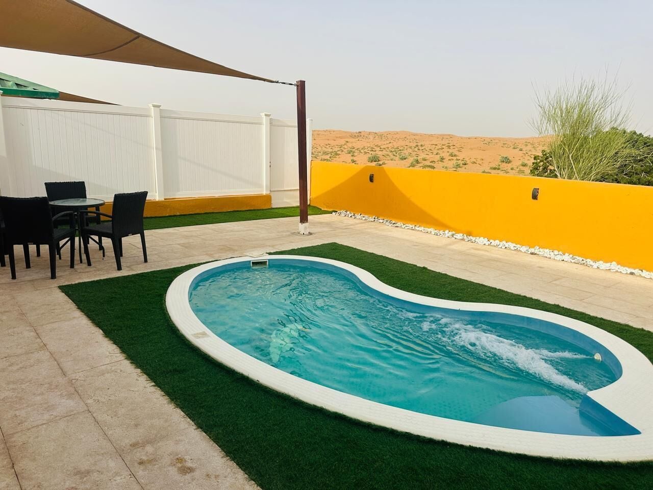 A swimming pool with a white border, surrounded by artificial grass, and a white fence.