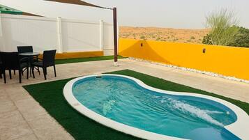 A swimming pool with a white border, surrounded by artificial grass, and a white fence.