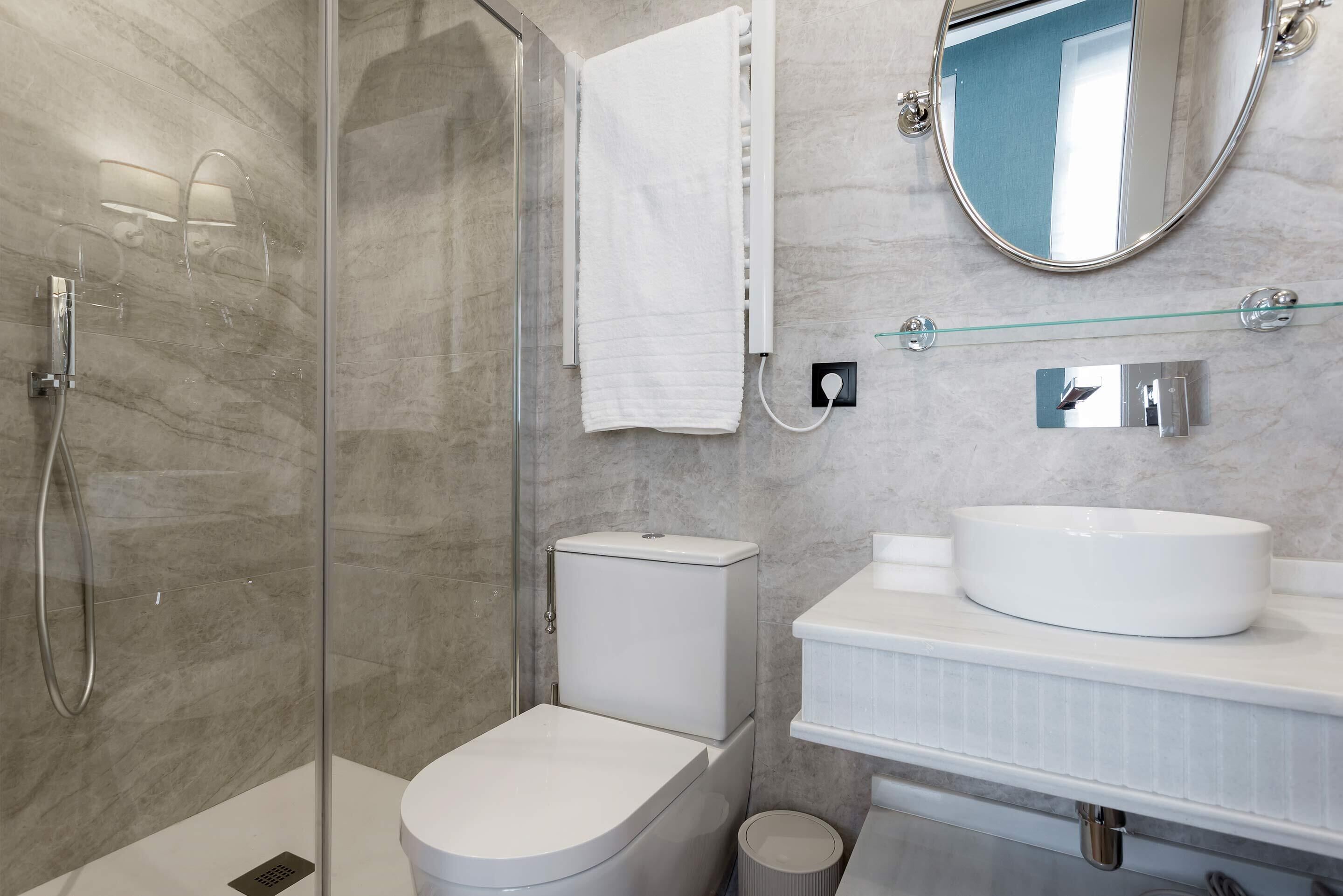 Un baño moderno con ducha de vidrio, inodoro, lavamanos con espejo y perchero para toallas.