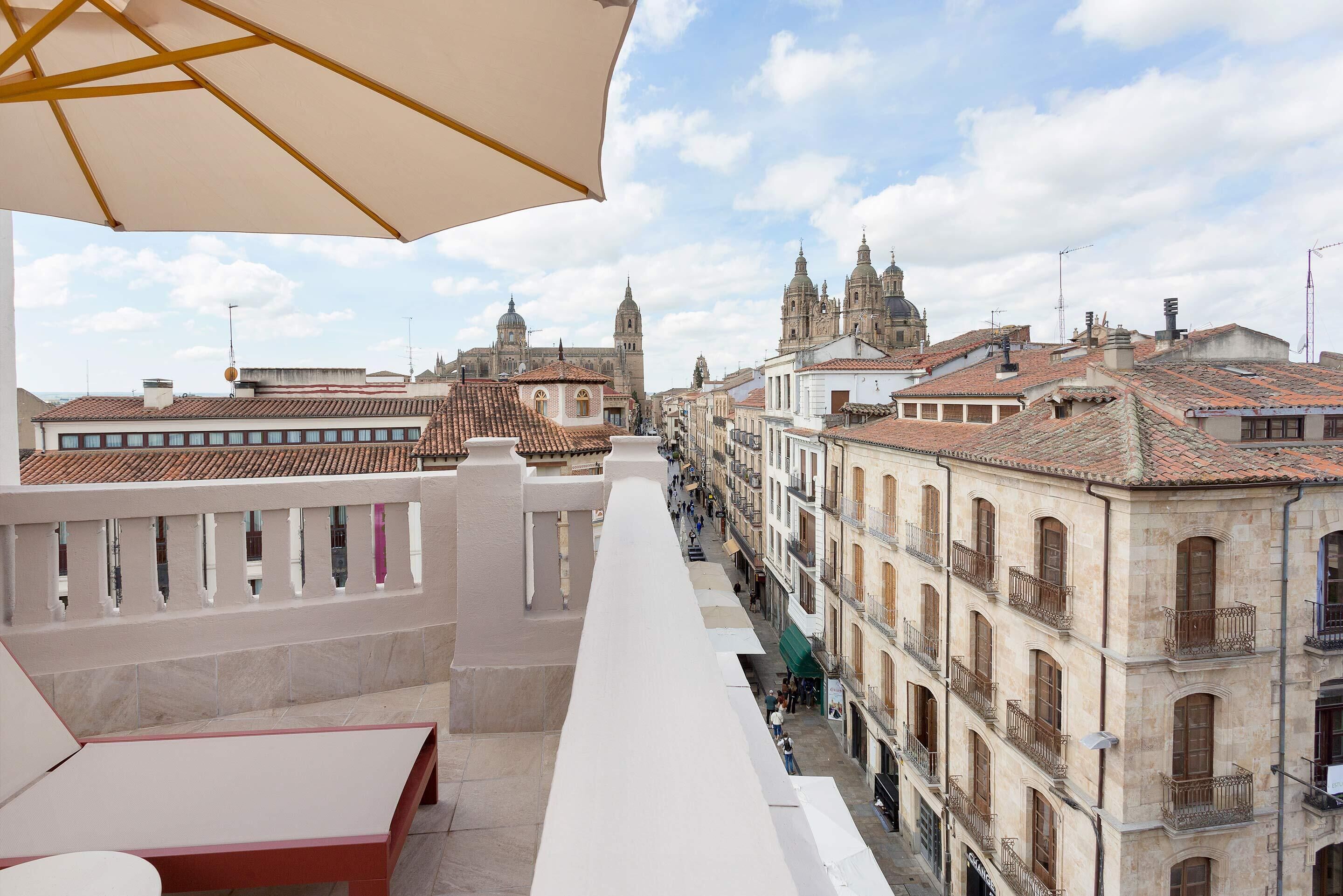 A terrace with a view of historic buildings, a table, and an umbrella.