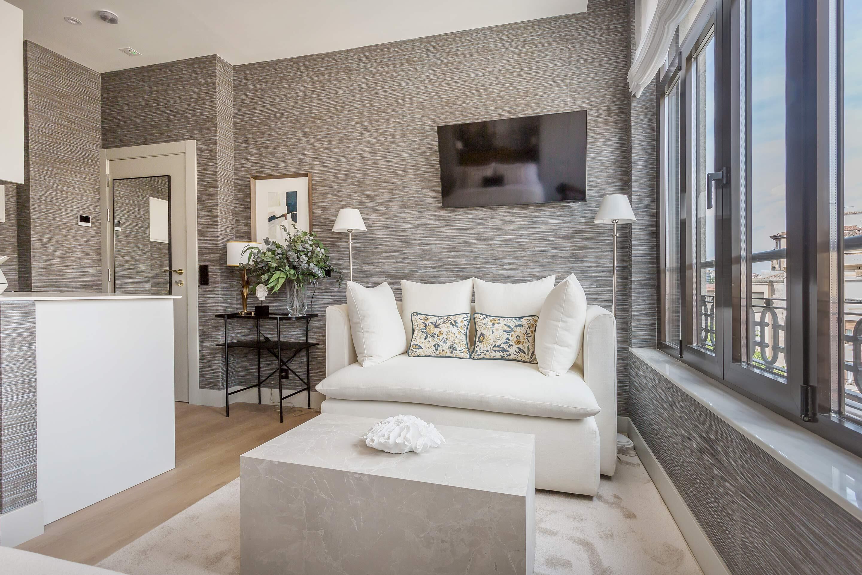 A modern living room with a white sofa, a coffee table, and a large window with a view.
