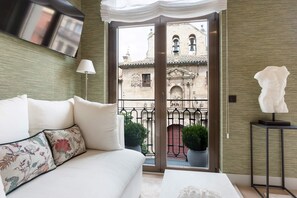 A modern hotel room with a sofa, a flat-screen TV, a balcony with potted plants, and a view of historic buildings. - Genteel Home Isla de la Rua Salamanca (Salamanca)