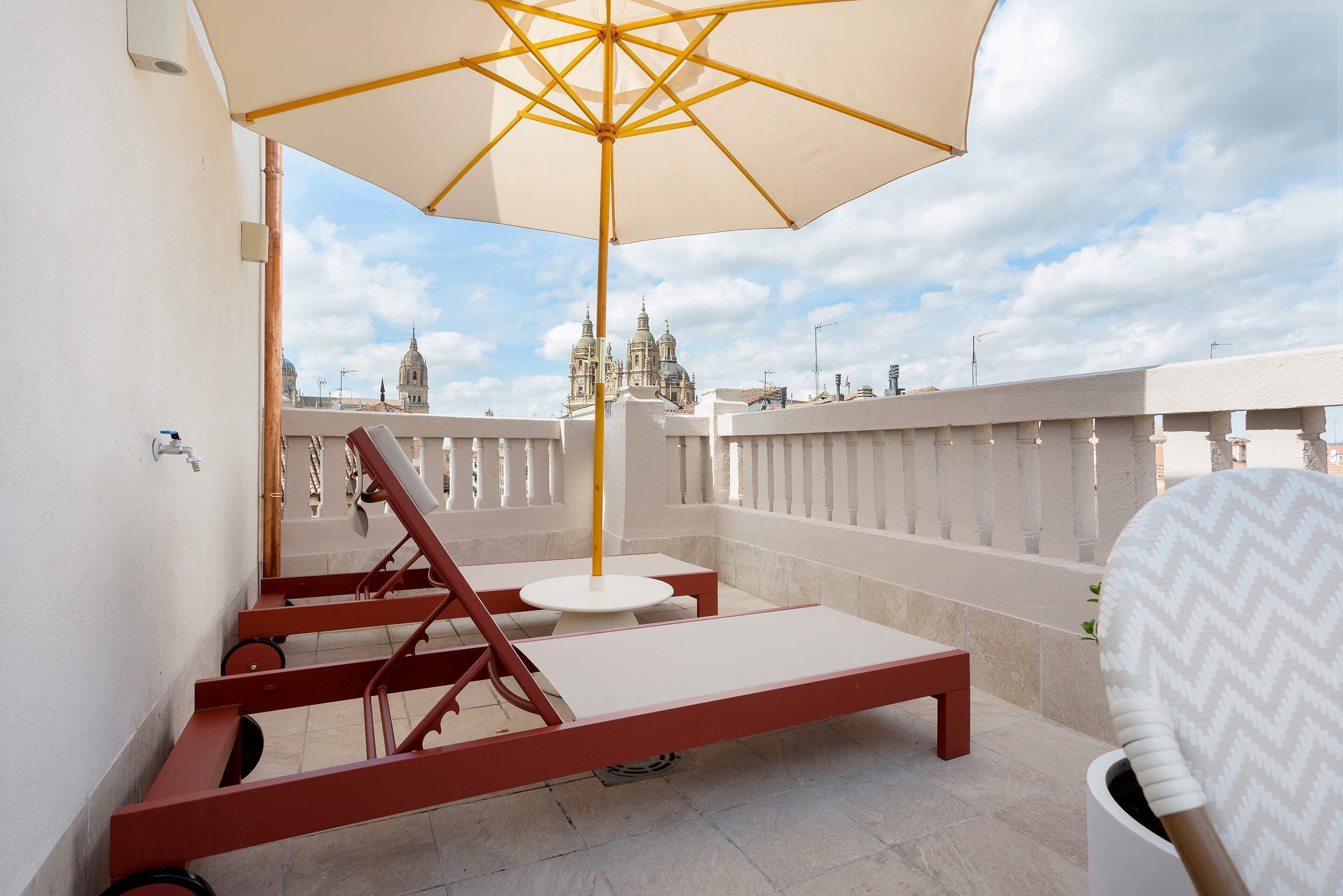 Un balcon avec un parasol blanc, un banc rouge et une chaise.