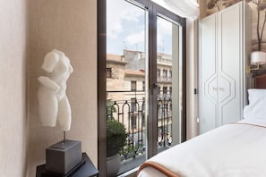 Una habitación de hotel con cama, una escultura, vistas a edificios y una puerta.