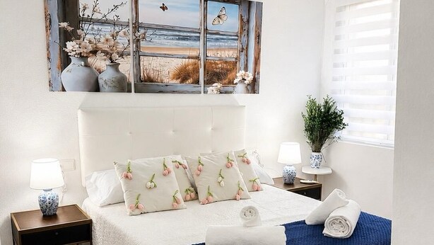 A bedroom with a bed, nightstands, a window with blinds, and a painting above the bed. - Centrally located two-bedroom apartment with patio. Charming (Córdoba España)
