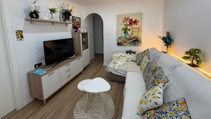 A modern living room with a flat-screen TV, sofa, coffee table, and artwork on the walls. - Centrally located two-bedroom apartment with patio. Charming (Córdoba España)