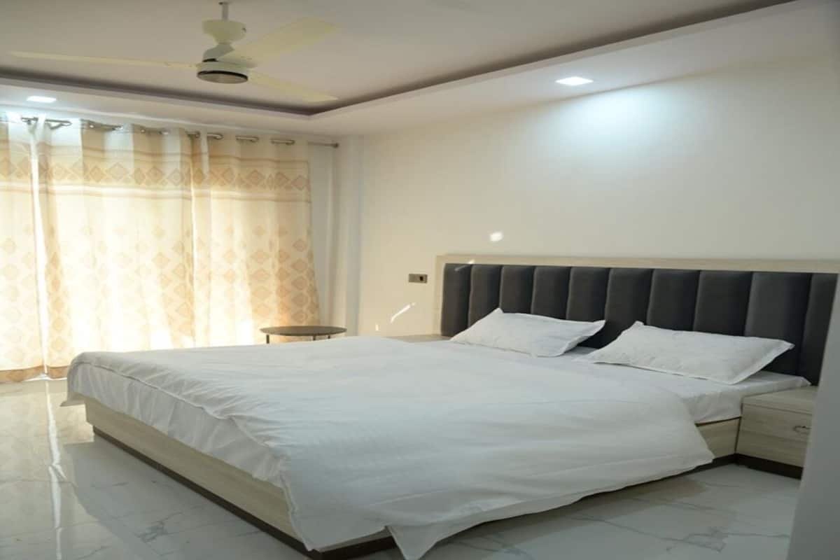 A bedroom with a large bed, a bedside table, a ceiling fan, and a window with curtains.
