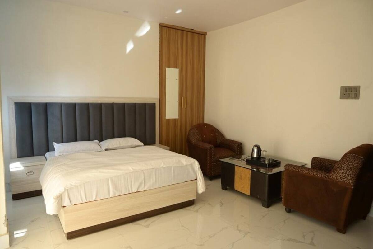 A hotel room with a large bed, a wooden wardrobe, a small table, two armchairs, and a mirror.