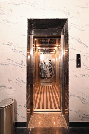 An elevator with a digital display, marble walls, and a patterned floor.