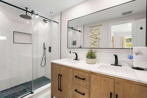 Ein modernes Badezimmer mit einer gläsernen Dusche, einem großen Spiegel und einem hölzernen Waschtisch mit weißer Arbeitsplatte.
