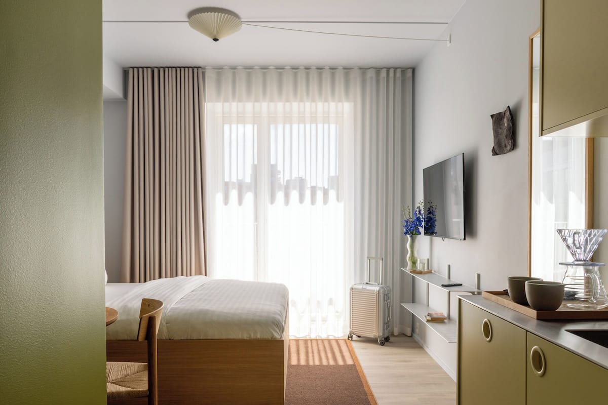 A hotel room with a bed, a desk, a TV, and a window with curtains.
