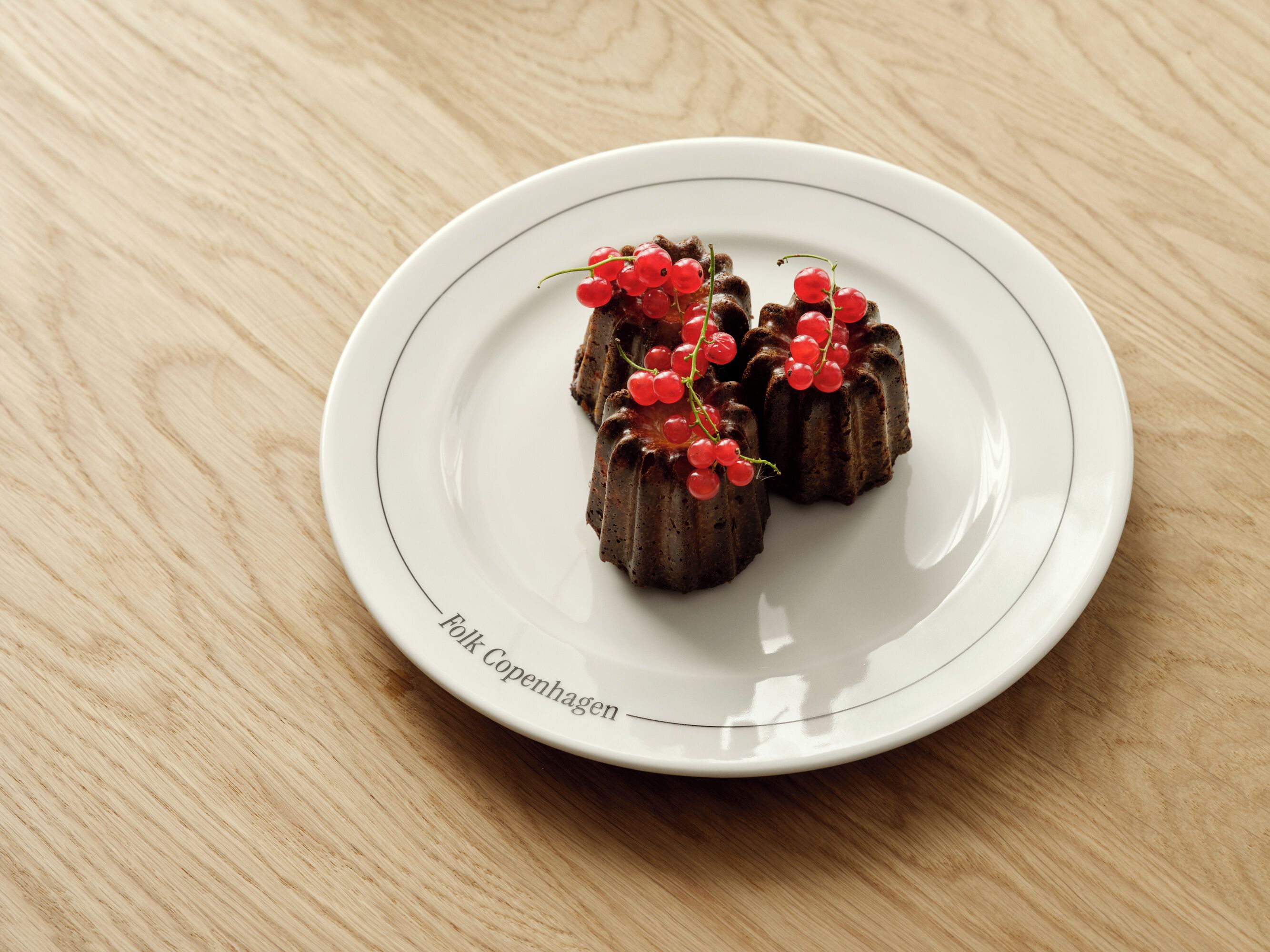 A white plate with three chocolate desserts and red currants on a wooden table.