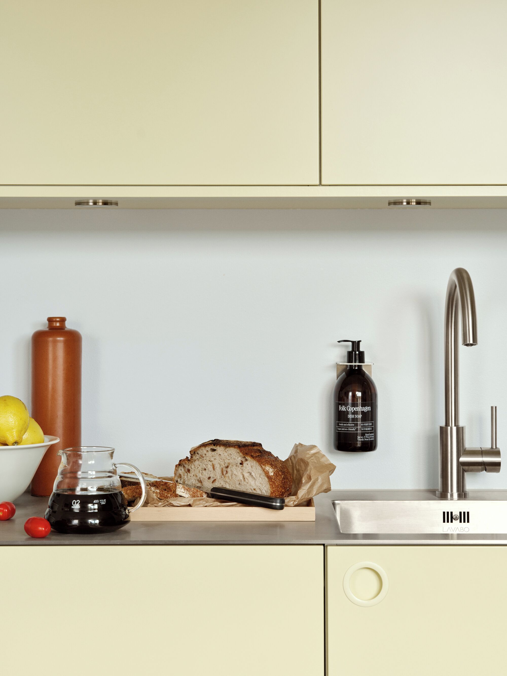 Una cocina con una hogaza de pan, una botella de detergente para platos y una tetera sobre la encimera.