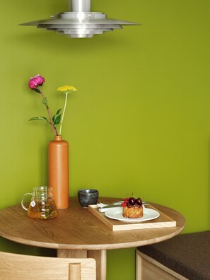 A round wooden table with a vase of flowers, a teapot, a bowl, and a plate with a dessert. - Folk Copenhagen (København)