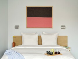 Una cama bien tendida con sábanas blancas, cabecera de madera y una bandeja con té y tazas sobre la cama.