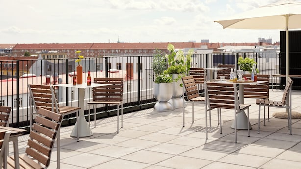 Eine Dachterrasse mit Sitzgelegenheiten im Freien, Topfpflanzen und Blick auf die Stadtlandschaft.