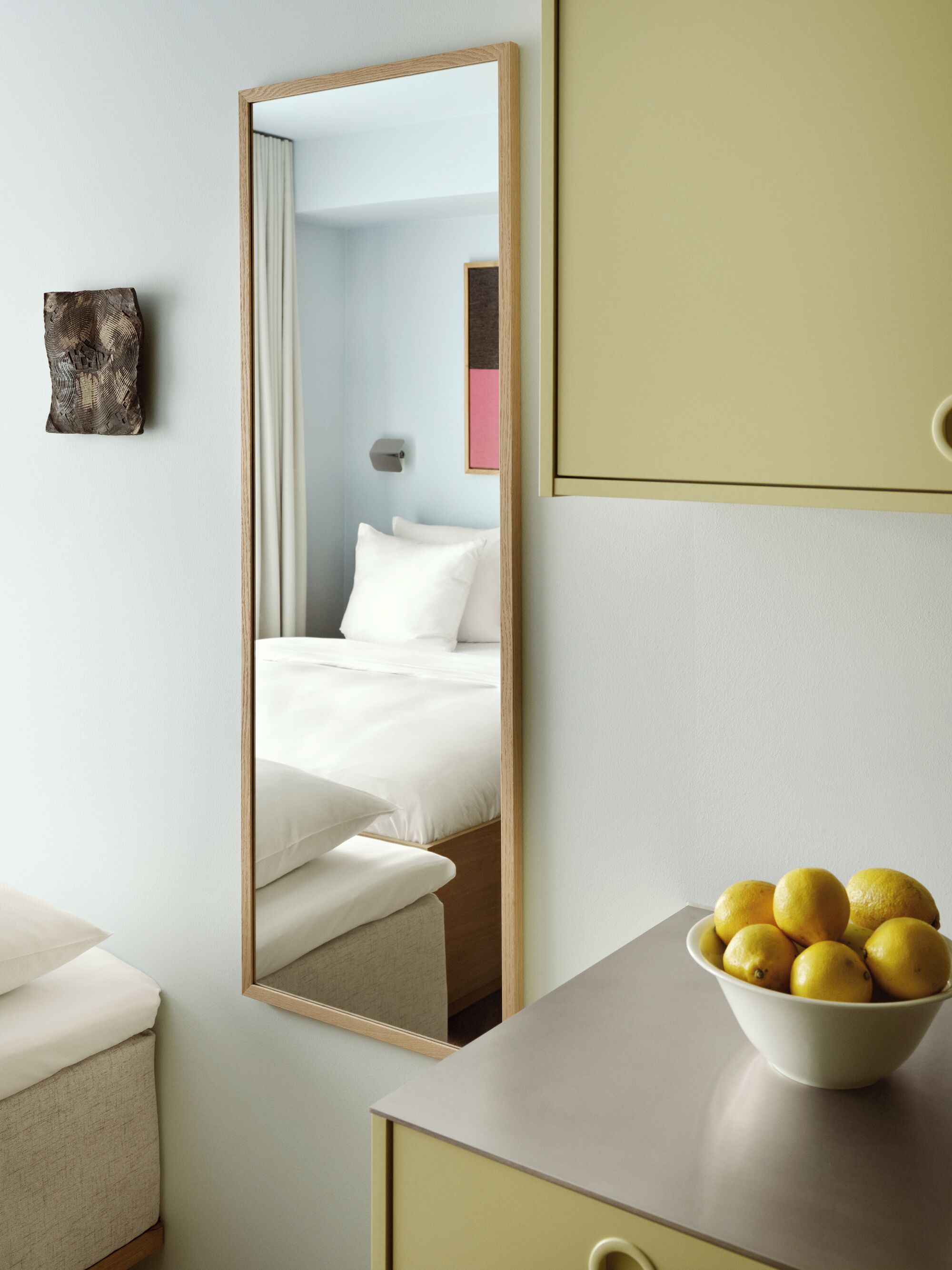 Una habitación de hotel con una cama, un espejo, una mesita de noche con un cuenco de limones y una pequeña obra de arte en la pared.